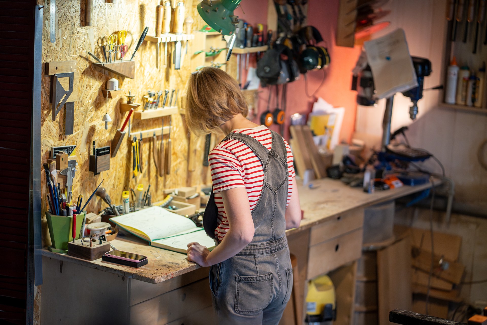Concentrated female carpenter at workbench drawing sketches of future wood furniture products.